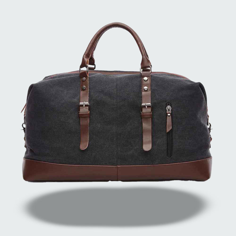 Sac de voyage en toile noire avec poignées et détails en cuir marron, fermeture éclair, poche avant zippée. Élégant et pratique pour le voyage.