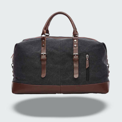 Sac de voyage en toile noire avec poignées et détails en cuir marron, fermeture éclair, poche avant zippée. Élégant et pratique pour le voyage.