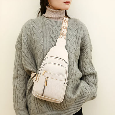 Sac à bandoulière beige porté par une femme en pull gris torsadé. Accessoire mode tendance avec fermeture éclair dorée et sangle décorative.