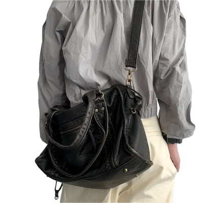 Personne portant un sac à main en cuir noir avec bandoulière, veste grise et pantalon beige. Mode, accessoires, style urbain.