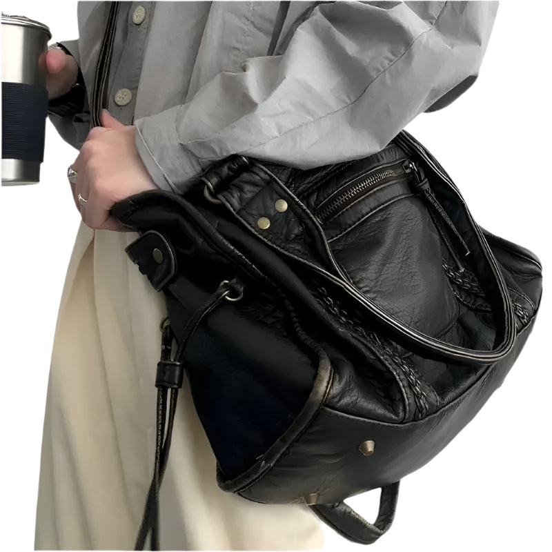 Sac à main en cuir noir porté par une personne en chemise grise, tenant une tasse de voyage. Mode élégante, accessoires tendance, style urbain.