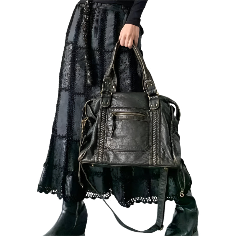 Femme tenant un sac à main en cuir noir texturé, jupe longue noire en dentelle, bottes noires. Mode élégante, accessoires tendance.