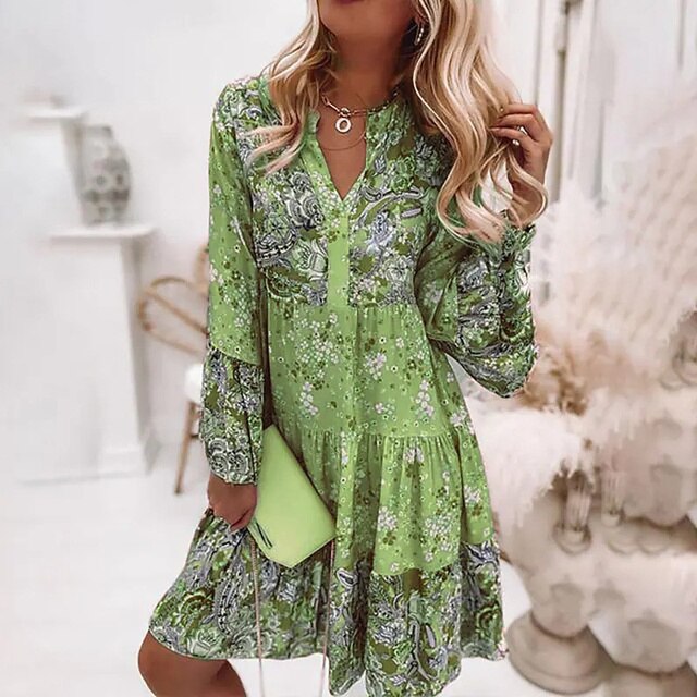 Robe verte à motifs floraux portée par une femme blonde, tenant une pochette verte. Mode féminine élégante, style printanier, tenue décontractée.