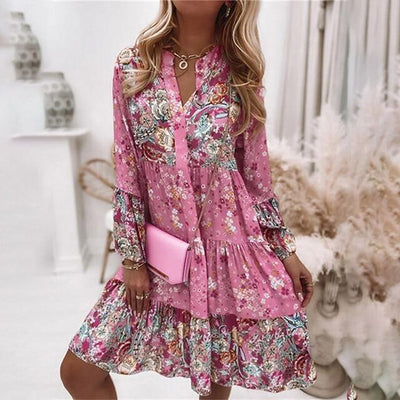 Robe fleurie rose à manches longues, tenue élégante pour femme, accessoirisée d'une pochette rose, style bohème chic, intérieur lumineux.