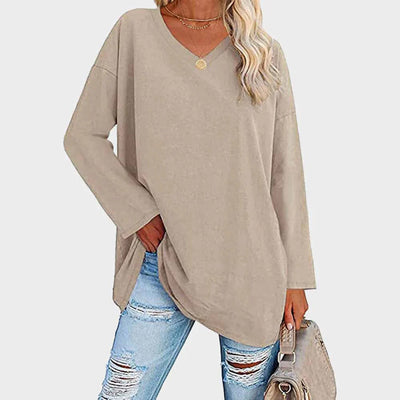 Femme portant un pull beige ample avec un col en V, associé à un jean déchiré bleu clair et un sac à main beige. Mode décontractée élégante.