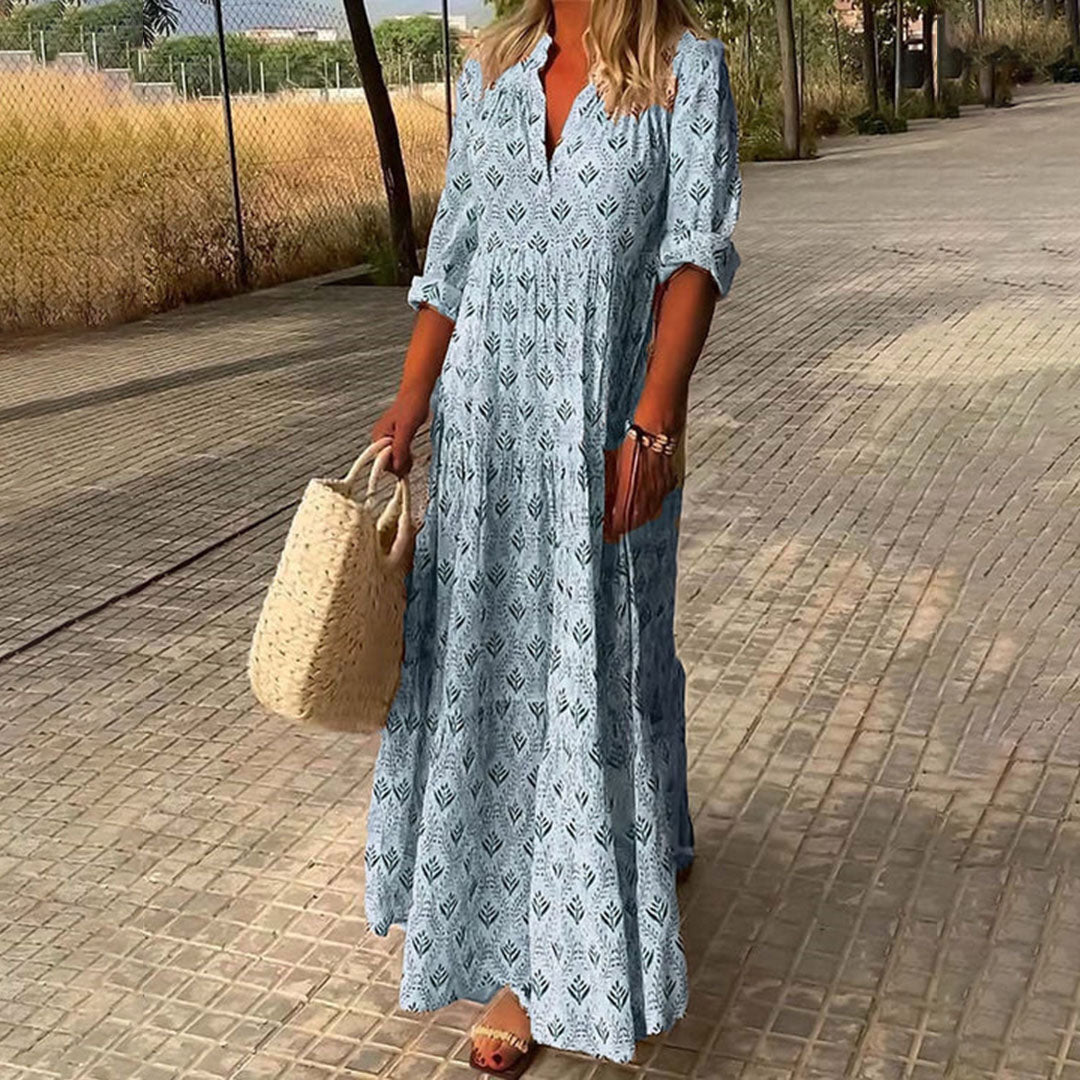 Robe longue bohème bleue à motifs géométriques, femme tenant un sac en osier, marchant sur un chemin pavé, style estival décontracté.