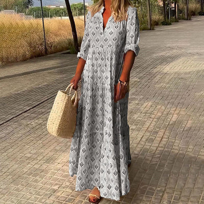 Femme en robe longue à motifs géométriques, portant un sac en osier, marchant sur un chemin pavé. Mode estivale, style bohème chic.