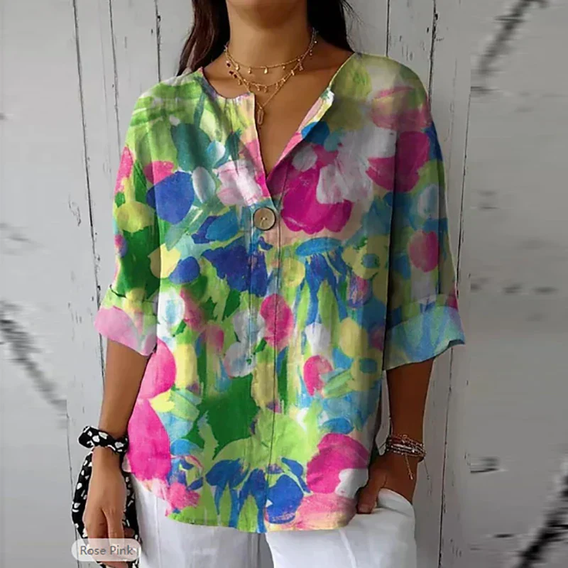 Blouse femme colorée à motifs floraux, manches trois-quarts, col en V, bouton central, portée avec un pantalon blanc. Mode printemps-été tendance.
