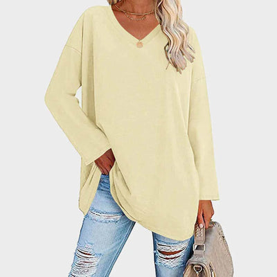 Femme portant un pull beige à col en V, manches longues, avec un jean déchiré et un sac à main beige. Mode décontractée, tendance automne.