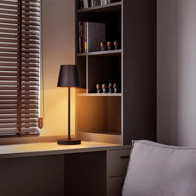 Lampe de bureau moderne allumée sur un bureau en bois, étagères avec figurines, store en bois, ambiance chaleureuse, design intérieur contemporain.