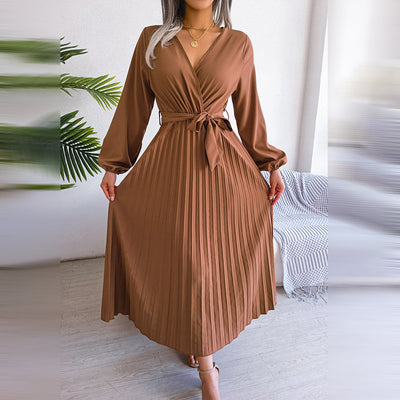 Robe longue plissée marron avec ceinture, manches longues, col en V, portée par une femme. Élégante tenue automne-hiver, mode féminine chic.