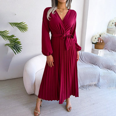Robe longue plissée bordeaux avec ceinture, manches longues, portée par une femme dans un salon moderne. Élégance, mode féminine, tenue chic.