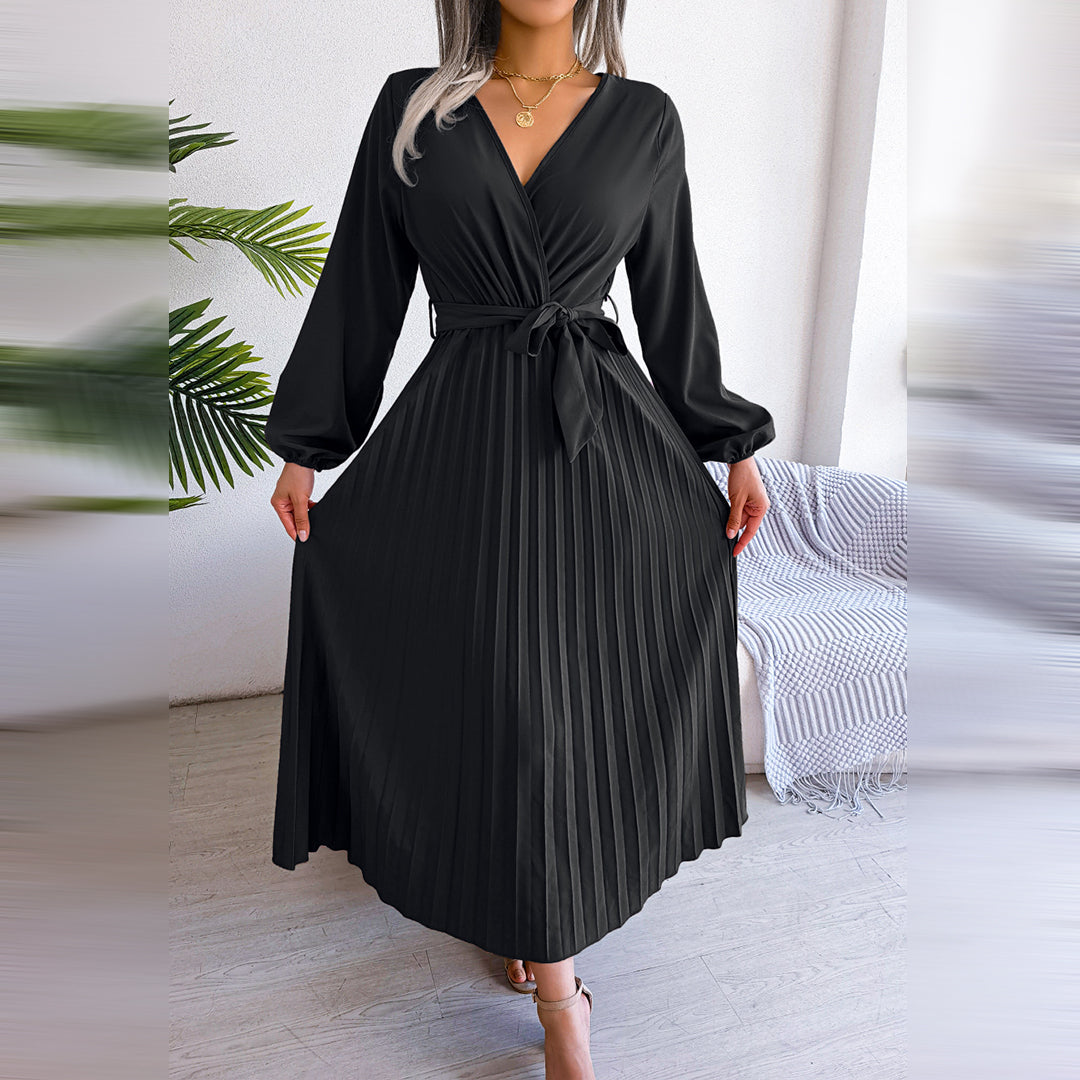 Robe noire élégante à manches longues et ceinture, plissée, portée par une femme dans un intérieur moderne avec plantes vertes. Mode féminine chic.