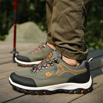 Chaussures de randonnée vertes pour homme sur plancher en bois, avec semelles antidérapantes et lacets orange, idéales pour activités de plein air.