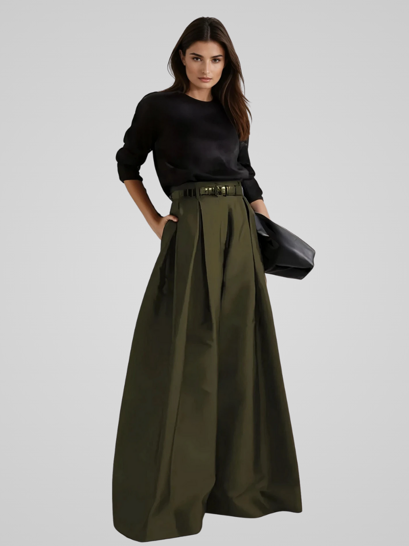 Femme portant une jupe longue verte taille haute avec ceinture, associée à un haut noir à manches longues. Mode élégante et moderne.