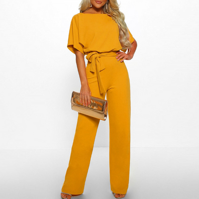 Femme en combinaison jaune élégante avec ceinture, tenant une pochette dorée. Mode féminine chic, tenue de soirée tendance.