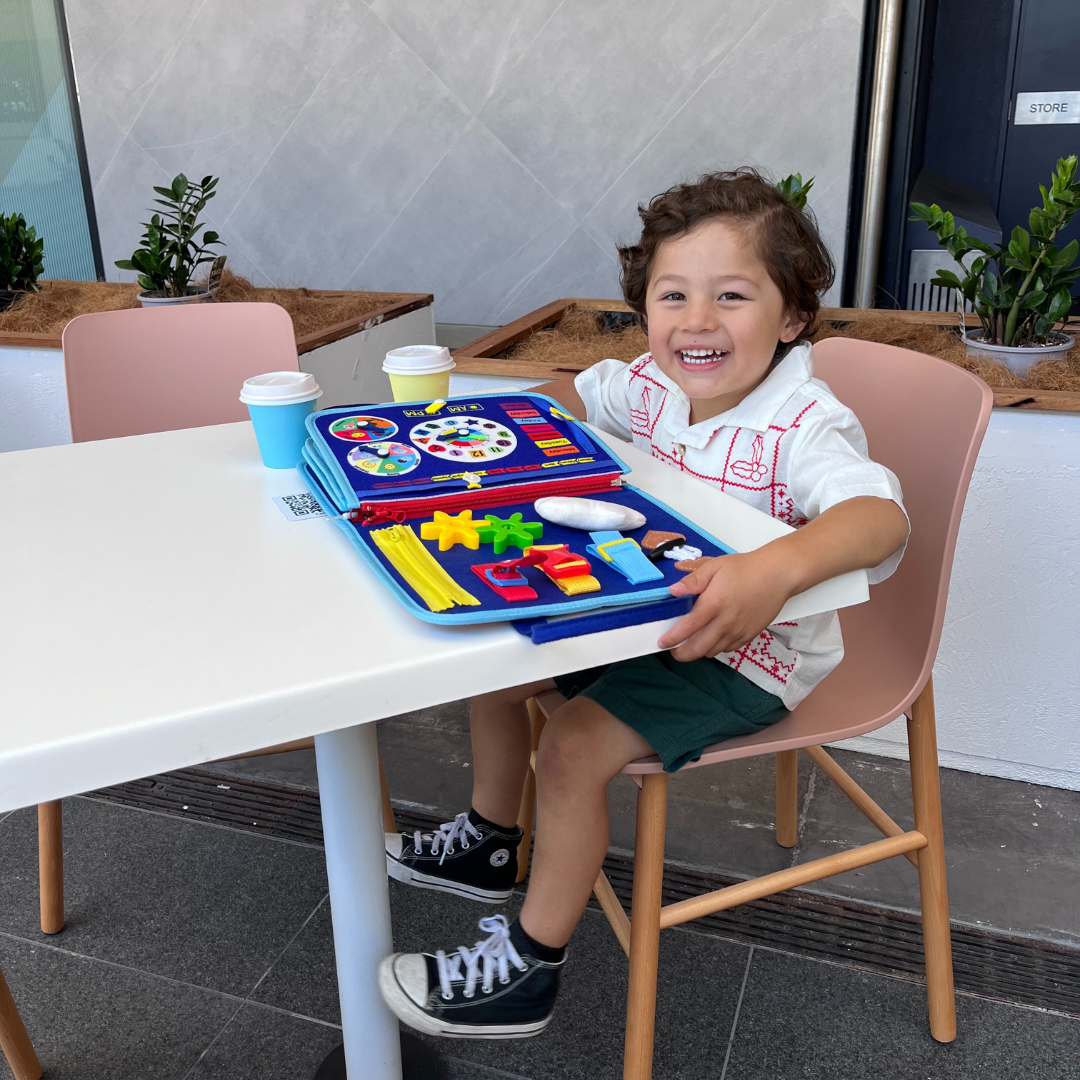 Enfant souriant jouant avec un jouet éducatif coloré sur une table de café, gobelets en carton à côté, ambiance moderne et lumineuse.