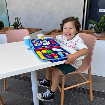 Enfant souriant jouant avec un jouet éducatif coloré sur une table de café, gobelets en carton à côté, ambiance moderne et lumineuse.