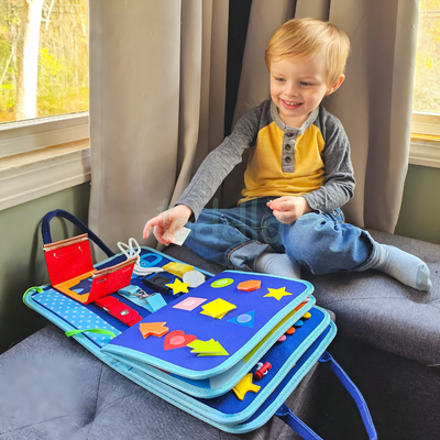Enfant jouant avec un livre d'activités éducatif en tissu, rempli de formes colorées et d'outils d'apprentissage, près d'une fenêtre lumineuse.
