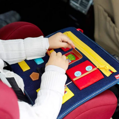 Enfant jouant avec un livre d'activités en tissu coloré dans une voiture, développant la motricité fine et l'apprentissage sensoriel.