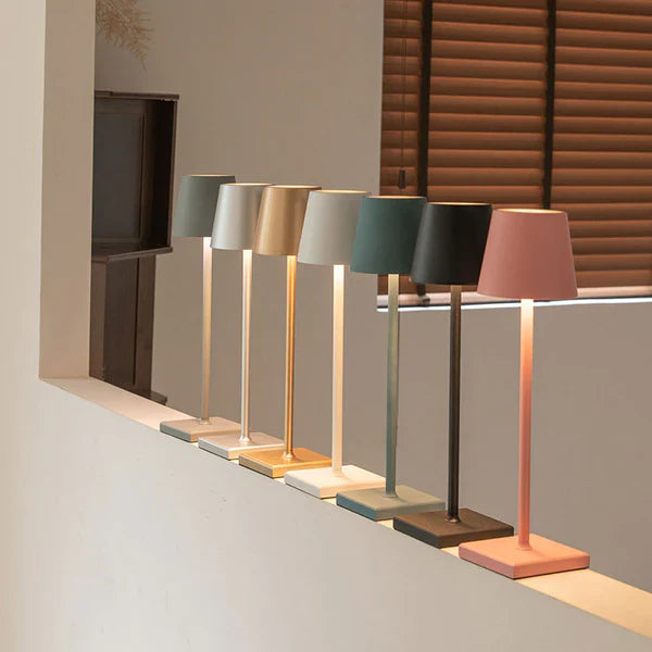 Sept lampes de table modernes alignées sur une étagère, avec abat-jours colorés en rose, vert et beige, éclairant un intérieur minimaliste et élégant.