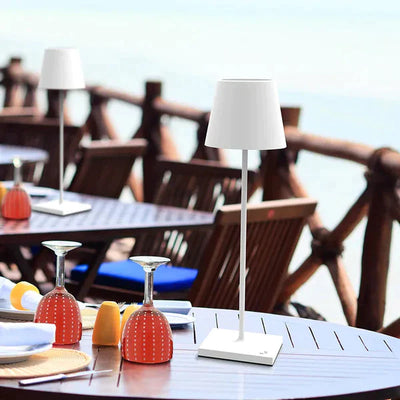 Lampe de table blanche moderne sur terrasse en bois, vue mer. Design élégant, éclairage extérieur, ambiance détente, restaurant bord de mer.
