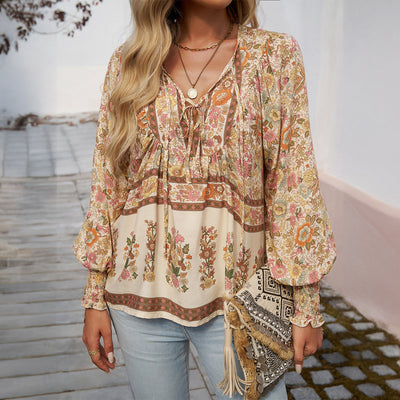 Femme portant une blouse bohème à motifs floraux, manches longues bouffantes, avec un sac à franges, sur fond de rue pavée. Mode bohème chic.