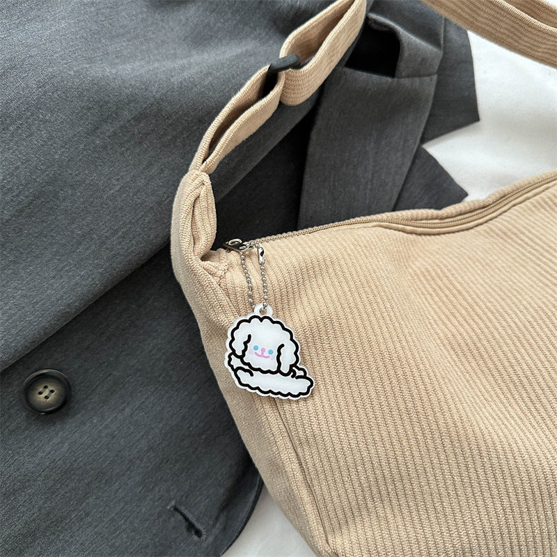 Sac beige en tissu côtelé avec porte-clés nuage mignon, posé sur un manteau gris. Accessoire mode tendance, style kawaii, design original.
