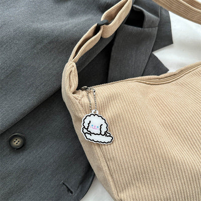 Sac beige en tissu côtelé avec porte-clés nuage mignon, posé sur un manteau gris. Accessoire mode tendance, style kawaii, design original.