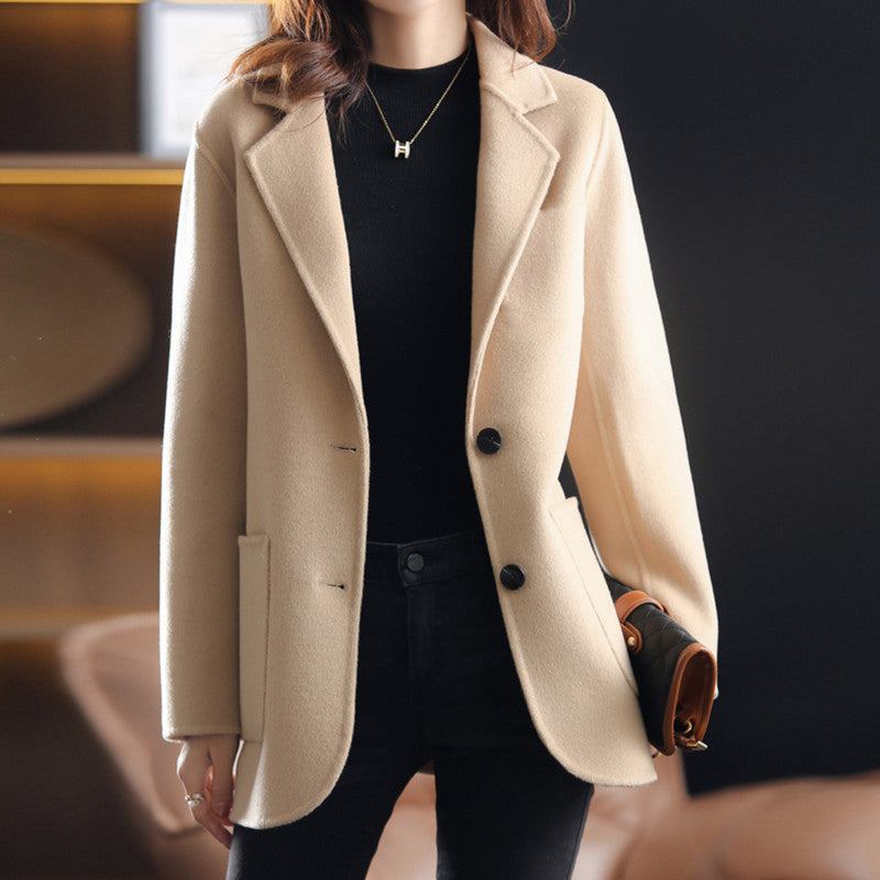 Femme portant un manteau beige élégant, col tailleur, boutons noirs, tenue chic automne-hiver, mode féminine moderne, intérieur sophistiqué.