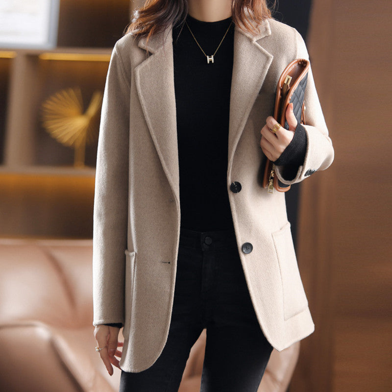 Femme portant un manteau beige élégant, tenue chic avec pull noir, tenant un portefeuille. Mode automne-hiver, style moderne et sophistiqué.