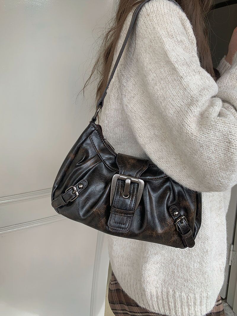 Femme portant un sac à main en cuir noir avec boucle métallique, tenue en laine beige. Mode automne, accessoire tendance, style élégant.