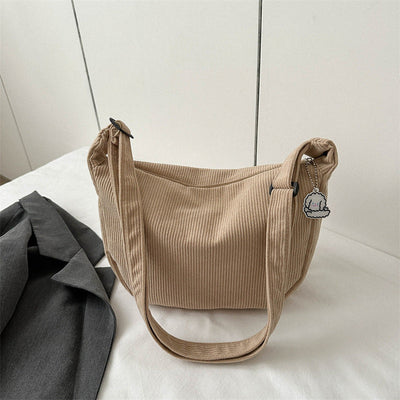 Sac à main beige en tissu côtelé avec breloque nuage, posé sur une surface blanche à côté d'une veste grise. Accessoire mode tendance.