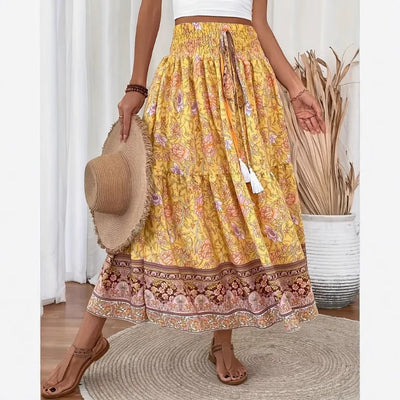 Jupe longue bohème jaune à motifs floraux, ceinture élastique, tenue estivale décontractée, femme tenant un chapeau de paille, sandales marron.