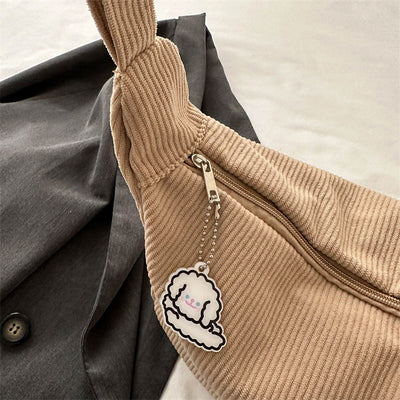 Sac en tissu côtelé beige avec fermeture éclair, orné d'un porte-clés nuage souriant. Posé sur une veste grise. Accessoire mode tendance.