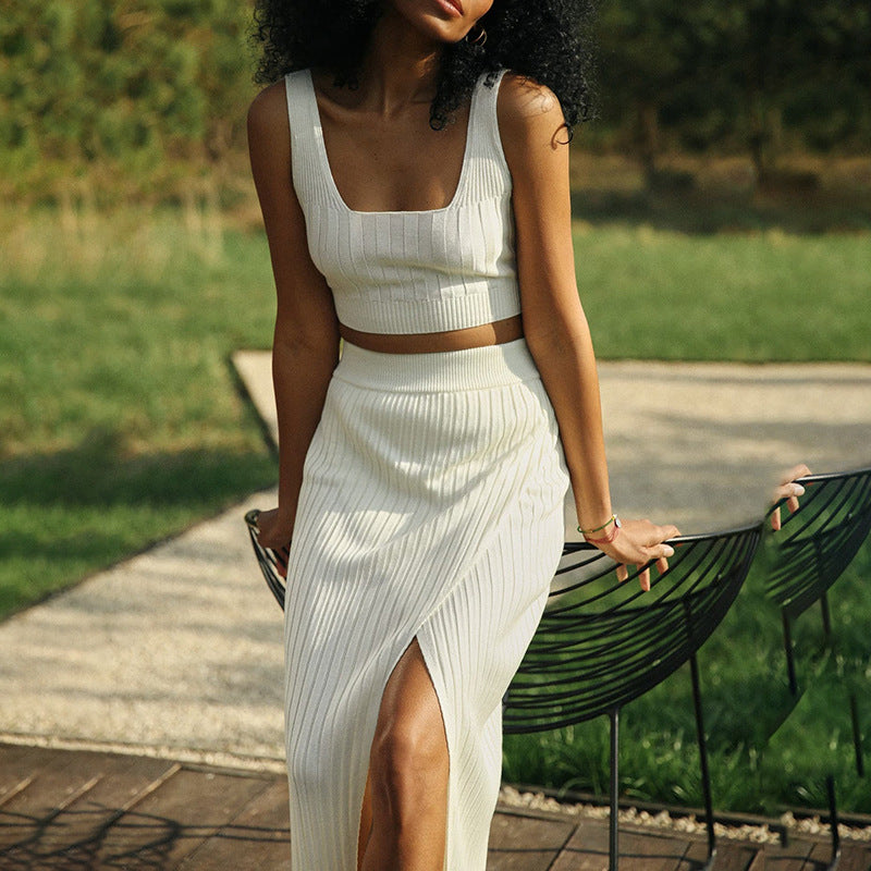 Femme en robe blanche élégante avec fente, posant dans un jardin verdoyant. Mode estivale, style chic, tenue décontractée.