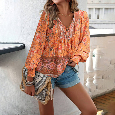 Femme en blouse orange à motifs floraux, short en jean, tenant un sac bohème. Mode estivale, style décontracté, tendance bohème chic.