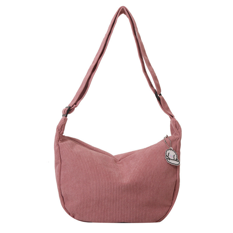 Sac à bandoulière rose en velours côtelé avec fermeture éclair et badge décoratif, mode femme, accessoire tendance, style décontracté.