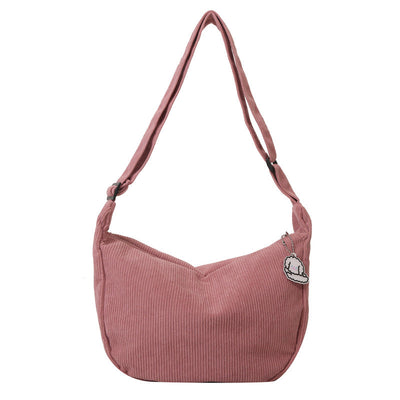 Sac à bandoulière rose en velours côtelé avec fermeture éclair et badge décoratif, mode femme, accessoire tendance, style décontracté.