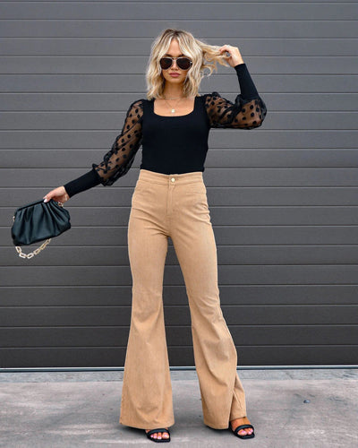 Femme en tenue chic: pull noir à manches transparentes, pantalon beige évasé, lunettes de soleil, sac noir. Mode élégante et tendance.