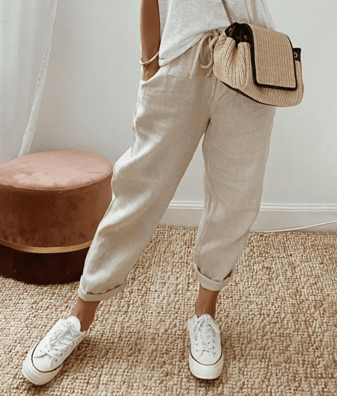 Pantalon en lin beige décontracté, porté avec un t-shirt blanc, des baskets blanches et un sac en osier, style mode estivale chic et confortable.