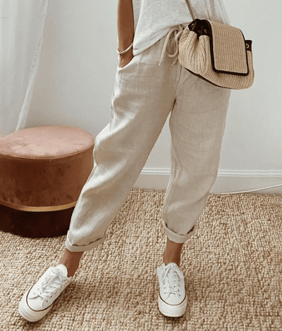 Pantalon en lin beige décontracté, porté avec un t-shirt blanc, des baskets blanches et un sac en osier, style mode estivale chic et confortable.
