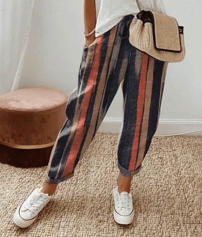 Pantalon à rayures multicolores, style décontracté, porté avec un sac en paille et des baskets blanches, mode féminine tendance.