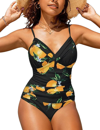 Femme en maillot de bain une pièce noir à motifs d'oranges, portant un chapeau de paille, souriante sous le soleil. Mode plage été.