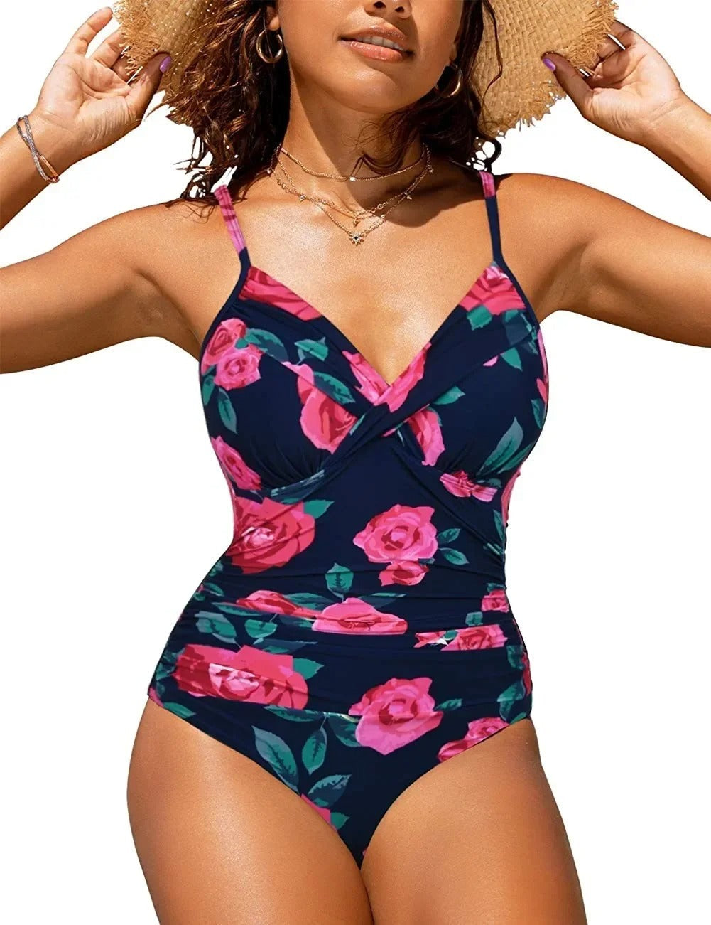 Femme portant un maillot de bain une pièce à fleurs roses sur fond bleu marine, style croisé, bretelles fines, accessoirisé d'un chapeau de paille.