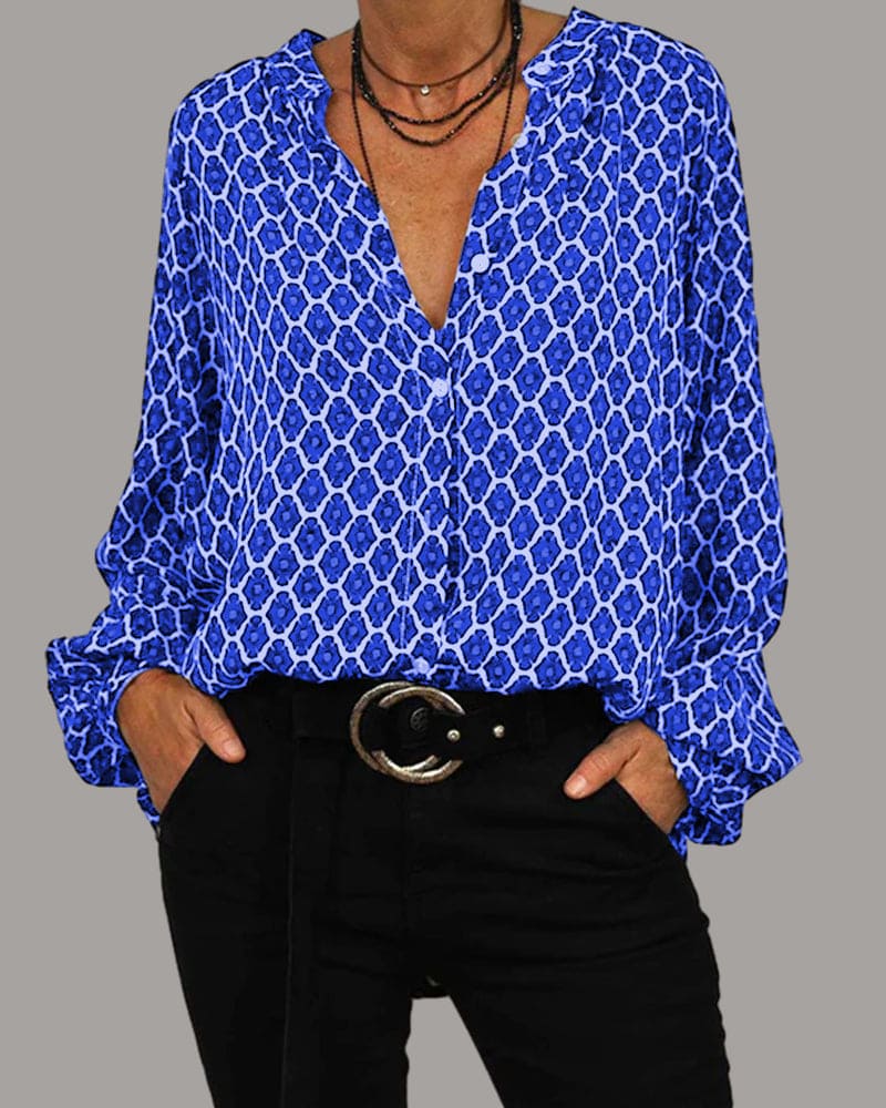 Chemisier bleu à motifs géométriques, manches longues, col en V, porté avec un pantalon noir et ceinture. Mode féminine élégante et tendance.