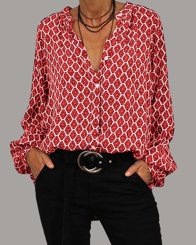 Chemisier rouge à motifs géométriques blancs, manches longues, col en V, porté avec un pantalon noir et ceinture, style mode femme élégante.