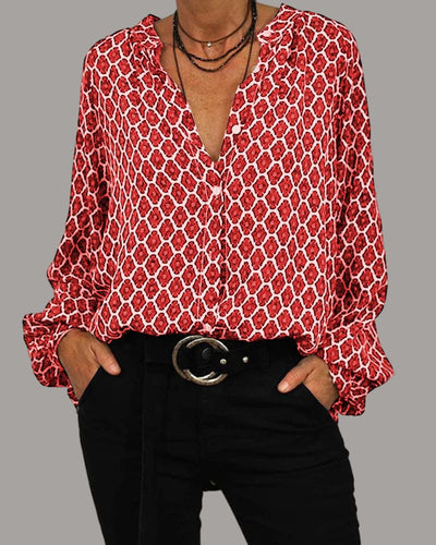 Chemisier rouge à motifs géométriques blancs, manches longues, col en V, porté avec un pantalon noir et ceinture, style mode femme élégante.