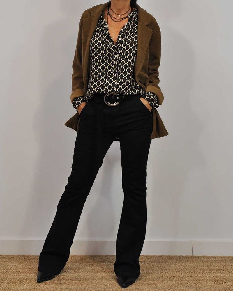 Femme en tenue chic: chemisier à motifs, blazer marron, pantalon noir évasé, ceinture avec boucle, colliers superposés. Mode élégante automne.