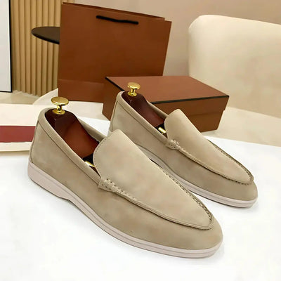 Mocassins en daim beige pour homme sur table blanche, avec embauchoirs dorés, boîtes en arrière-plan. Chaussures élégantes et modernes.